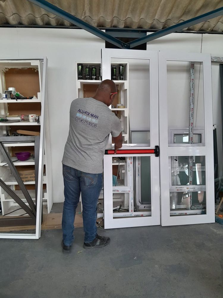 An installer checking white aluminium double doors with a push bar in the workshop